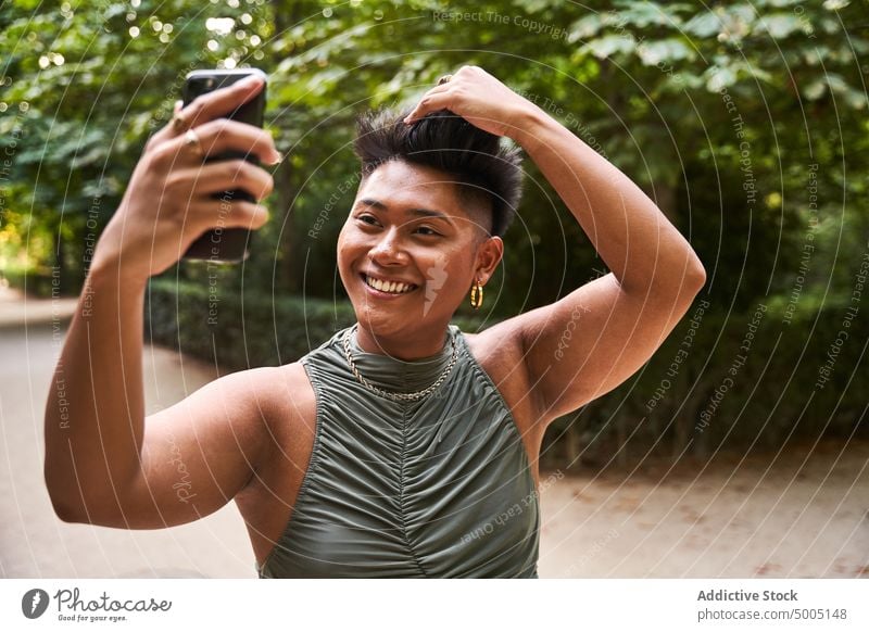 Fröhliche asiatische nicht-binäre Person, die ein Selfie macht Frau Transgender Lächeln Park Smartphone Haare berühren bewundern Reflexion & Spiegelung Glück