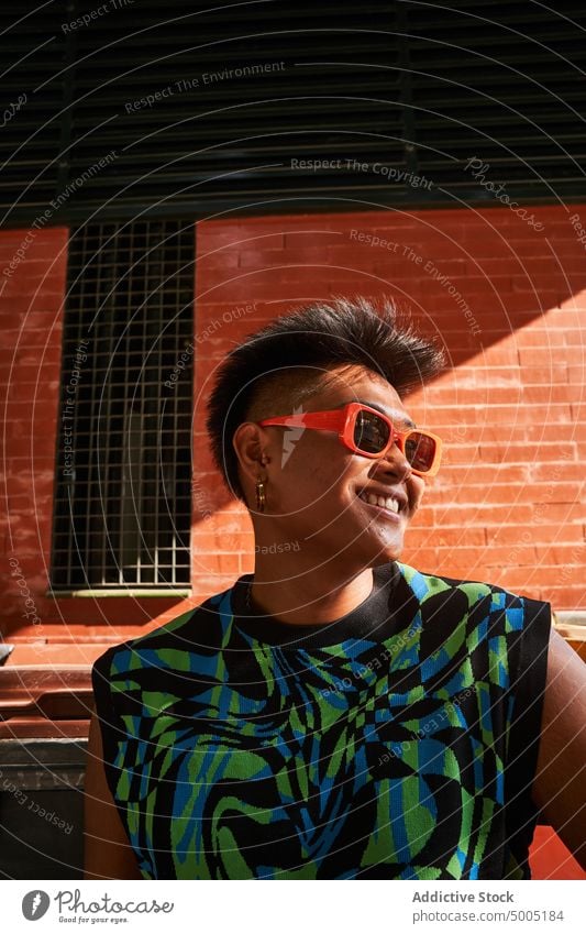 Fröhliche asiatische Transgender-Frau an der Mauer Lächeln Glück Backsteinwand urban nicht binär Stil Straße Vorschein Filipinos ethnisch unverfälscht