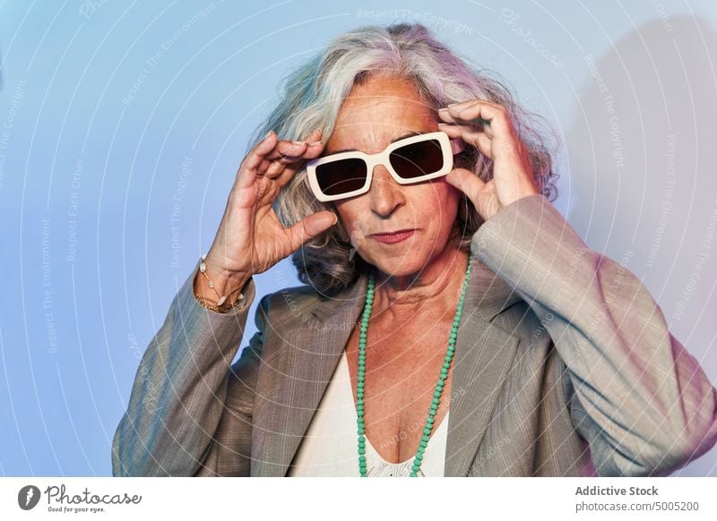 Stilvolle ältere Geschäftsfrau unter Neonlicht selbstbewusst leuchten neonfarbig ernst Touch-Sonnenbrille Vorschein Porträt smart lässig Frau gealtert Senior