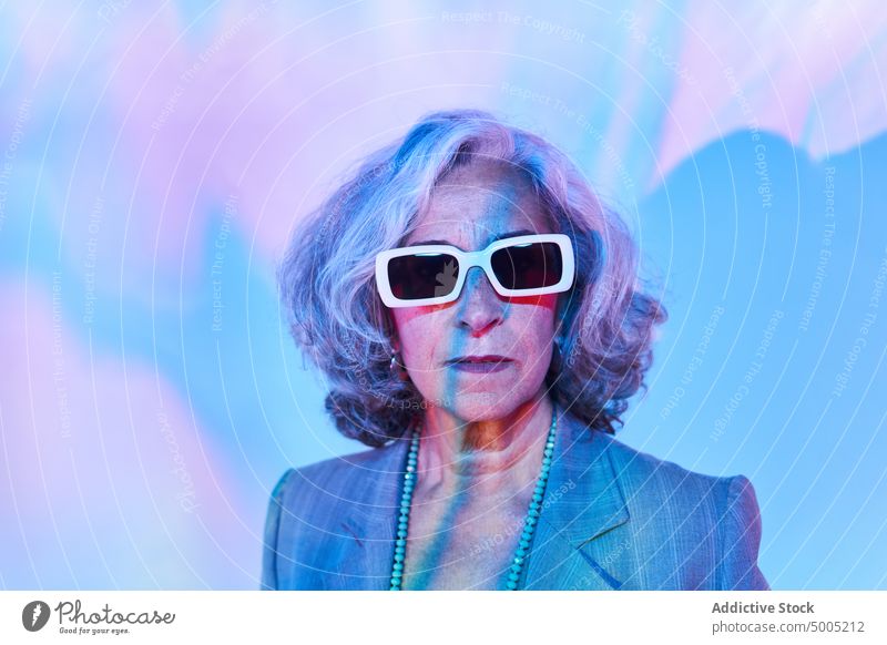 Ältere Frau unter buntem Neonlicht Rentnerin neonfarbig leuchten farbenfroh Individualität Porträt graues Haar älter Senior gealtert Halskette Jacke