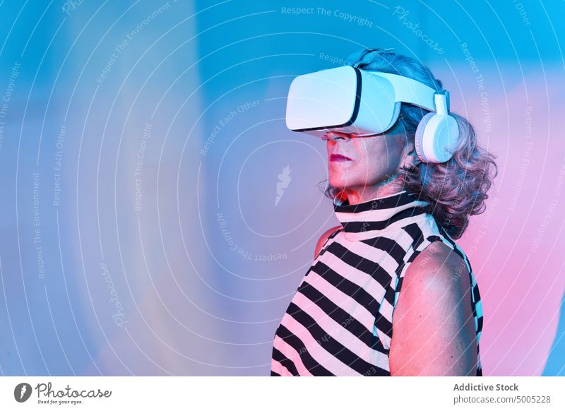 Stilvolle ältere Frau im VR-Headset erkunden Virtuelle Realität neonfarbig farbenfroh leuchten Spieler Erfahrung Cyberspace Senior gealtert Rentnerin