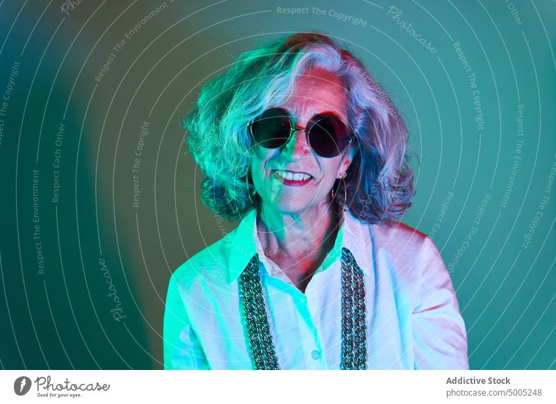 Stilvolle ältere Frau mit runder Sonnenbrille Lächeln Vorschein leuchten neonfarbig farbenfroh Porträt hell modern graues Haar Senior gealtert Rentnerin