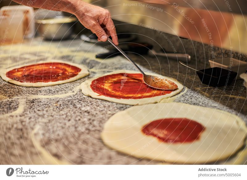 Crop-Koch beim Pizzabacken im Restaurant Mann Küchenchef Tomate Saucen Schliere Tradition vorbereiten männlich Löffel Aufstrich Bestandteil italienische Küche