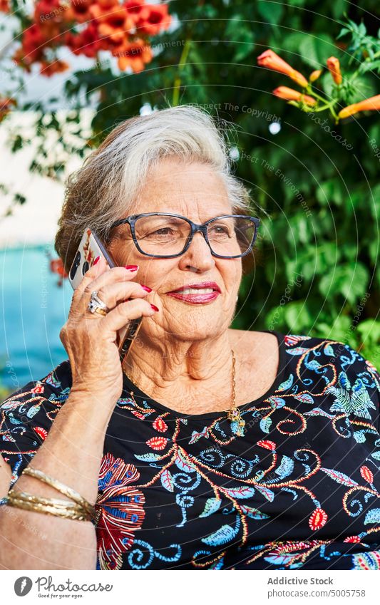 Ältere Frau spricht im Garten mit ihrem Smartphone reden Gespräch Lächeln Hof Blume Telefonanruf älter Senior gealtert sprechen Buchse Apparatur grün Sommer