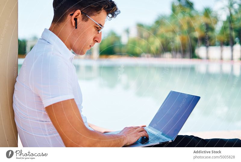 Seriöser Student, der mit seinem Smartphone spricht und auf seinem Laptop tippt Schüler männlich benutzend Universität Campus beschäftigt Mann Browsen Apparatur