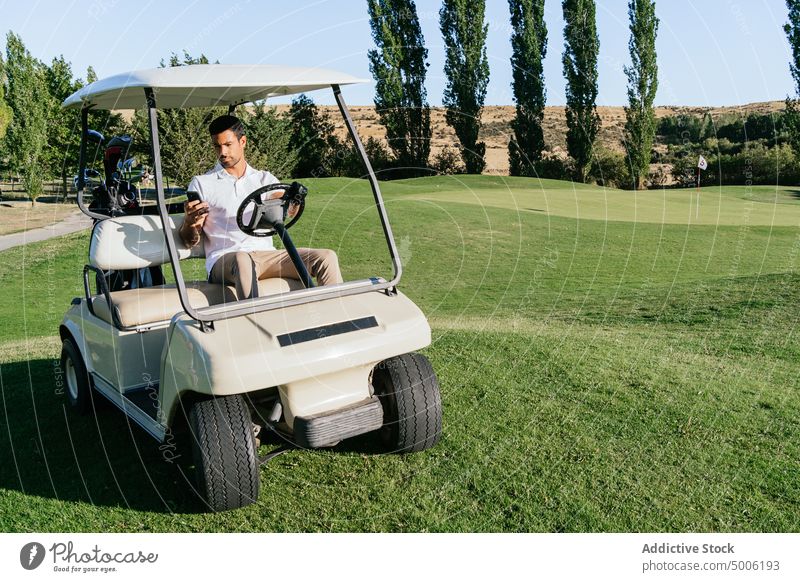 Golfer, der im Golfwagen auf dem Lande mit seinem Smartphone telefoniert plaudernd Karre Internet Gerät Mann Kurs Porträt benutzend Apparatur aristokratisch