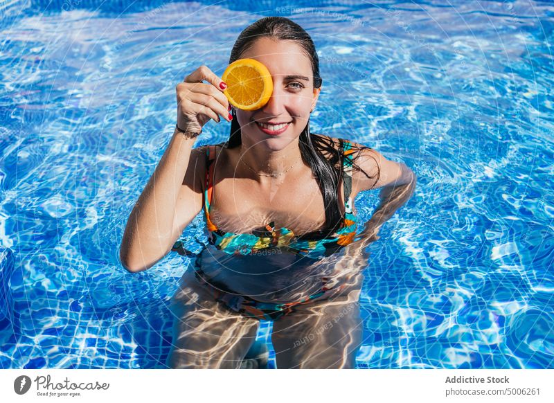 Glückliche Frau mit Orangenscheibe genießt den Sommer im Pool orange frisch tropisch Beckenrand Frucht Sonnenlicht Resort sonnig Wasser Urlaub heiter