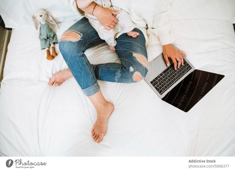 Anonyme Mutter, die den Computer mit Interesse benutzt, während sie mit ihrem Kleinkind zu Hause entspannt Laptop Baby Eltern Kind heimwärts heiter benutzend