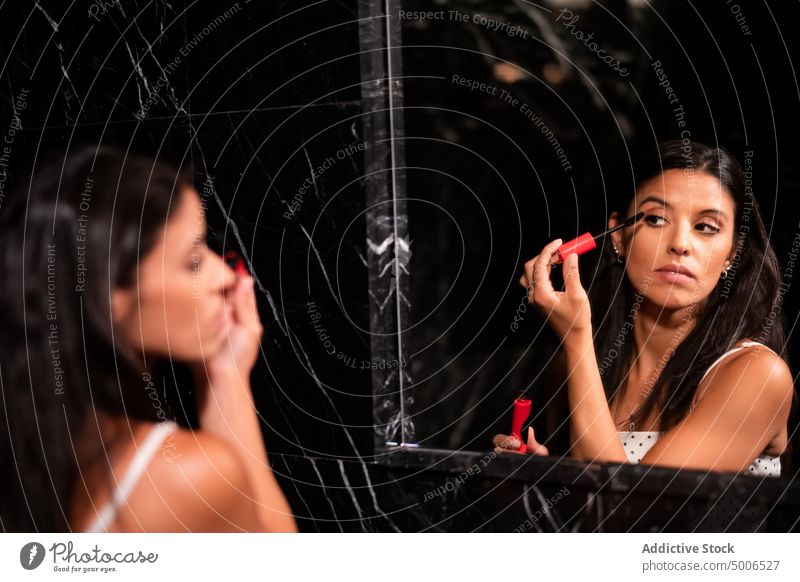 Konzentrierte junge Frau, die sich vor dem Spiegel schminkt angezogen Make-up bewerben Wimperntusche Bad Kosmetik Schönheit Mode vorbereiten feminin Werkzeug