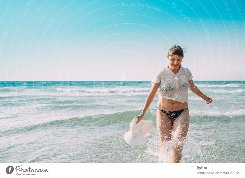 Junge kaukasische Frau Frau im Badeanzug und Sommerhut Laufen im Meer Wasser spritzt. Urlaub am Meer Ozean Strand Ägäis Spritzer aktiv aktiver Lebensstil