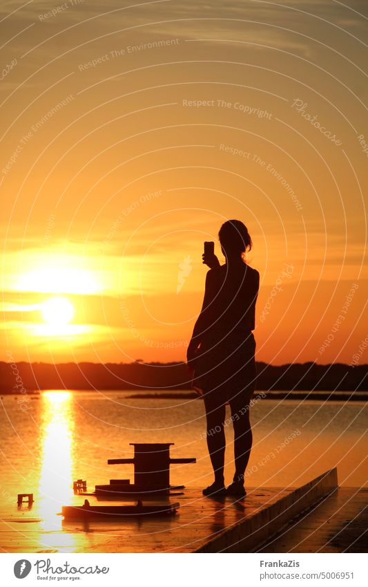 Frau fotografiert mit ihrem Smartphone den Sonnenuntergang über einer Lagune Abend Himmel Wasser Abenddämmerung Licht fotografieren Augenblick festhalten Sommer