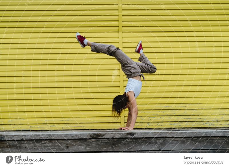 Junge Tänzerin in weißem Oberteil und Leinenhose macht einen Handstand vor der gelben Wand Frau im Freien Choreograph Mädchen stylisch urban Bewegung Menschen