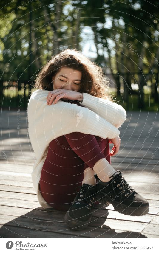 Lächelnde brünette Frau in einem weißen Pullover im Park sitzend, selektiver Fokus Erwachsener allein attraktiv Herbst lässig Kaukasier heiter krause Haare