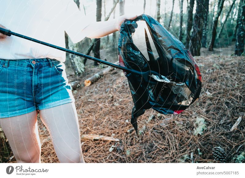 Foto von Seite des Mädchens Abholung Müll in Tasche auf den Wald während eines Sonnenuntergangs.Umweltmüll pollution.Nature Reinigung, freiwillige Ökologie grünes Konzept.