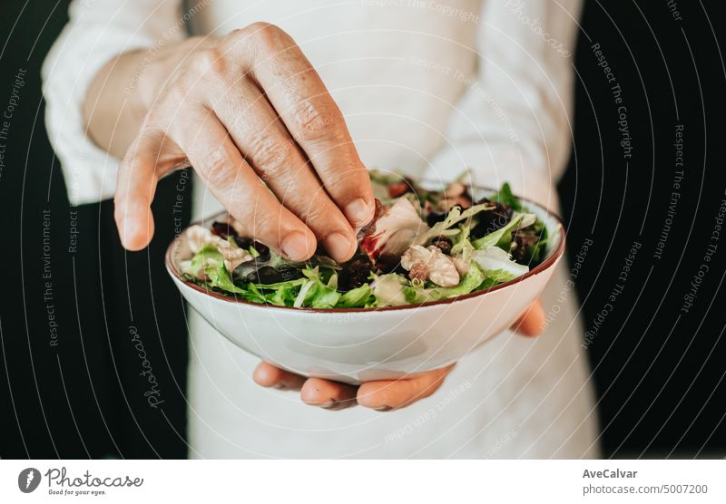 Alte Frau bei der Zubereitung von gesundem Essen, Salatrezept auf Schüssel. Zubereitung von Gemüse. Blick auf ältere Frau die Hände rühren den Salat mit einem Holzlöffel auf dem Tisch der Küche