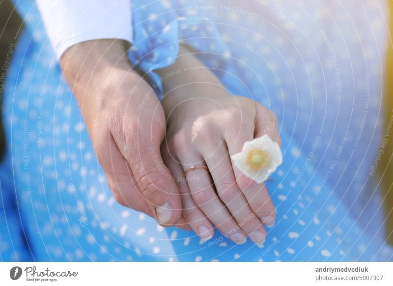 Romantisches Date-Konzept. Junger Mann und Frau halten sich an den Händen. Mädchen mit goldenem Ring am Finger in blauem Kleid mit Kamillenblüten in der Hand