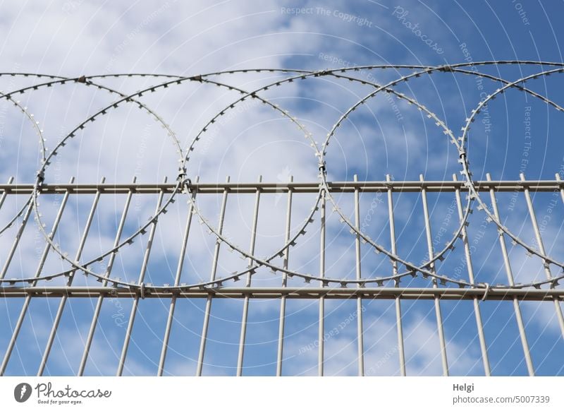 Kein Zutritt - hoher Metallzaun mit Stacheldraht vor blauem Himmel mit Wölkchen Zaun Draht Sicherung kein Zutritt Grenze Barriere Sicherheit Verbote Schutz