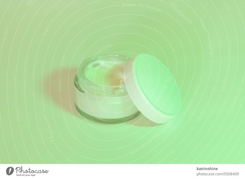 Geöffneter Kosmetiktopf mit Deckel in Nahaufnahme, Attrappe. Grünes Licht. Alltägliche Hautpflegeroutine Glas Sahne grün Schlagschatten weiß Negativraum
