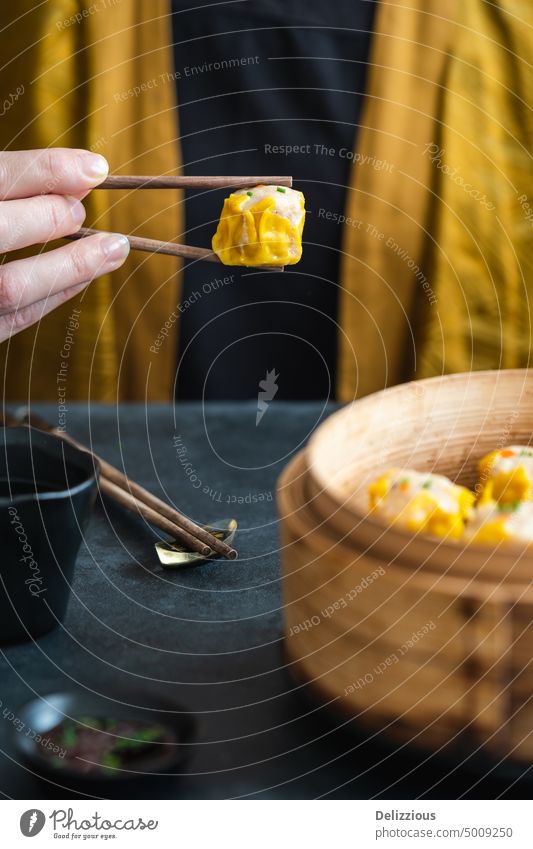 Eine Frau in gelbem Kimono hält ein Dim Sum mit Stäbchen asiatisch Anlasser Lebensmittel Genießer Amuse-Gueule eine Essstäbchen gedünstet gesonnt Verdunstung