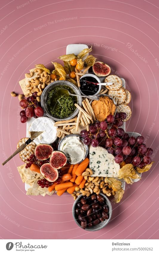 Eine schöne Käseplatte mit Obst, Gemüse, Dips und Nüssen auf einem rosa Hintergrund, vertikal Antipasti Holzplatte Camembert Karotten Käsesorten Nahaufnahme