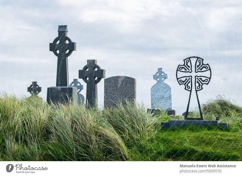 Irische Grabsteine auf einem grasbewachsenen Hügel am Meer friedhof grabmäler grabsteine irisch irland keltisch kreuze wiese hohes gras himmel wolken meer hügel