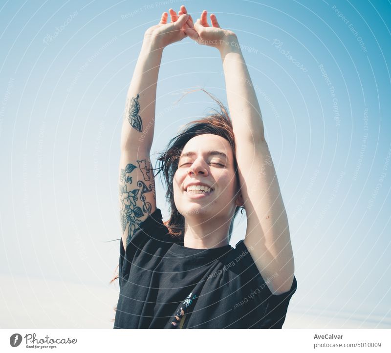 glückliche junge Frau, die die Freiheit genießt und die Arme in den Himmel streckt, während sie die Augen schließt. Blasen Haare und entspannen, Freiheit und Zukunft Konzept