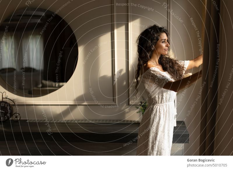 Junge Frau mit lockigem Haar steht am Fenster im Zimmer Appartement schön Schönheit lässig Kaukasier elegant genießen Gesicht Mode Weiblichkeit Spaß traumhaft