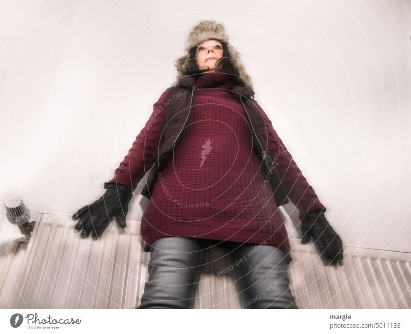 Eine Frau in Winterkleidung friert vor einer Heizung kalt frieren heizen Wärme Energie sparen Temperatur Heizkörper Heizungsregler thermostat Energiekrise teuer