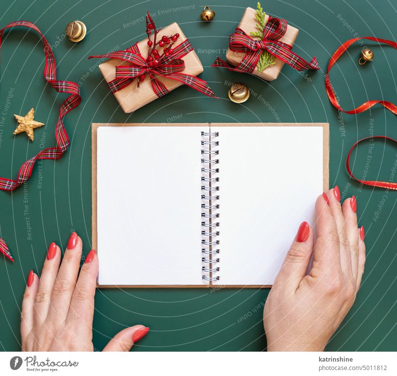 Hände mit Blank offenen Notizblock auf einem grünen Hintergrund in der Nähe von Weihnachtsgeschenken, Mockup Weihnachten Attrappe aufgeklappt Geschenkverpackung