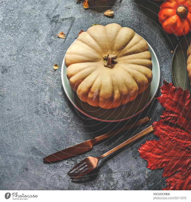 Gedeckter Tisch mit Kürbis auf Teller mit Besteck und Herbstblättern auf dunklem rustikalem Hintergrund, Ansicht von oben Tabelleneinstellung Herbstlaub dunkel