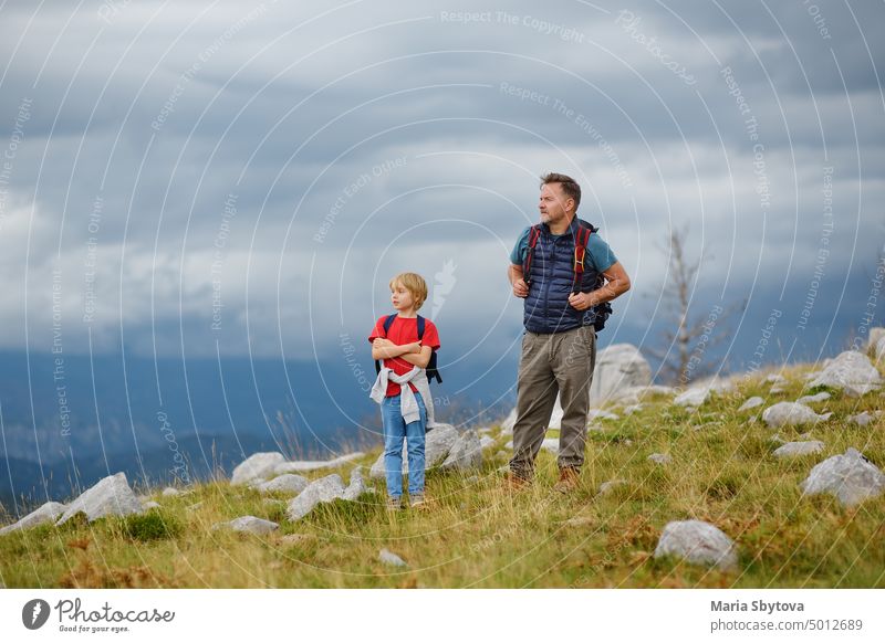 Niedliches Schulkind und sein reifer Vater wandern gemeinsam in den Bergen und erkunden die Natur. Konzepte von Abenteuer, Scouting und Wandertourismus für Kinder.
