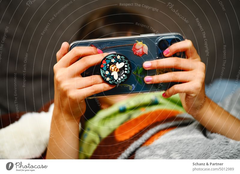 Kind mit lackierten Fingernägeln schaut auf ein mit Aufklebern beklebtes Smartphone Hände Hand festhalten Handy Streaming digital Internet social media Medien