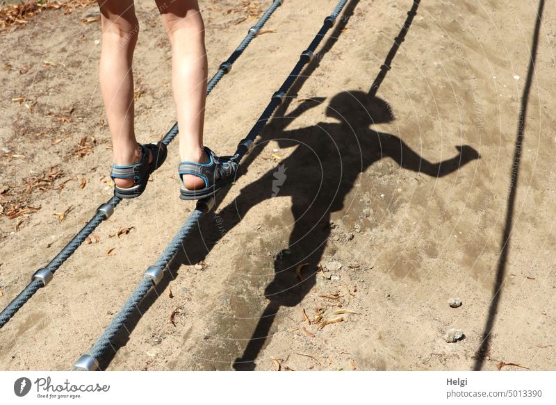 Junge balanciert auf einem Spielgerät, nur die Beine und ein Schatten des  Körpers sind zu sehen Kind Schulkind Körperschatten Seil balancieren Licht