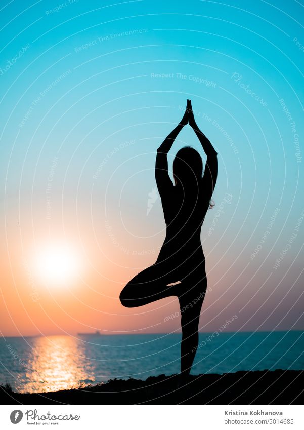 Junges schlankes Mädchen übt Yoga auf Berg gegen Ozean oder Meer bei Sonnenaufgang Zeit. Silhouette der Frau in Strahlen der awesome Sonnenuntergang. Strand