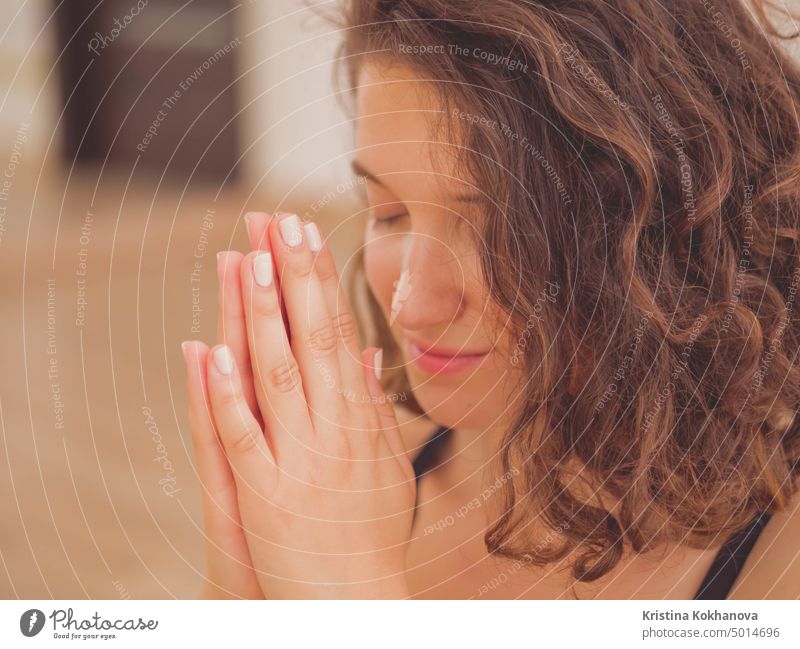 Junge schöne Frau mit kurzen lockigen Haaren meditiert im hellen Fitnessstudio. Hände in Namaste. Gebet, Dankbarkeit, Yoga, Liebe Gott Konzept. Mädchen jung