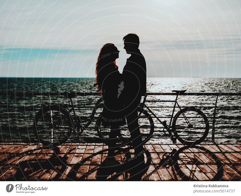 Silhouetten eines Paares in der Nähe von Fahrrädern am Meeresufer. Mädchen und Junge bei einem Date. Menschen und gesunder Lebensstil Konzept. Romantische Szene.