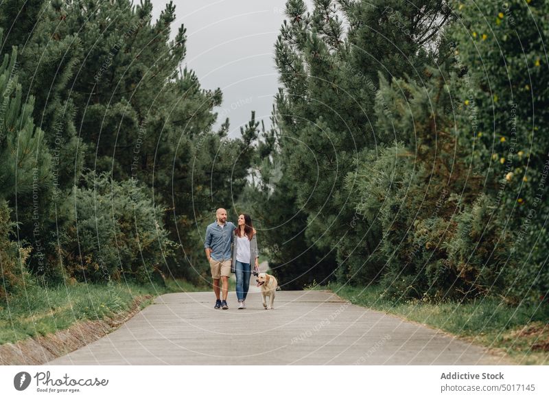Verliebte umarmen sich auf einem Fußweg im Wald mit Haustier Paar Umarmung Spaziergang Holz Glück erfreut Liebhaber Hund Freizeitkleidung Straße Zusammensein