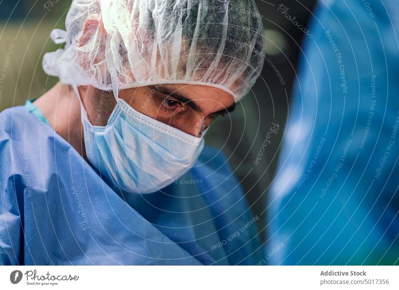 Chirurg mit Maske und chirurgischer Kappe während einer Operation Mann Mundschutz OP-Haube steril ernst Konzentration fokussiert nachdenklich Spezialist Klinik