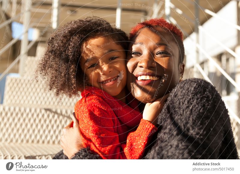 Lächelndes süßes schwarzes Mädchen umarmt Frau auf Stufen umarmend Mutter Schritt Straße Sonnenschein heiter Kind Tochter Treppe sonniger Tag Afroamerikaner