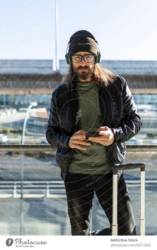Hipster-Mann surft auf dem Smartphone im Flughafen Telefon Browsen zuschauend reisen Passagier trendy Stil Erwachsener Lächeln positiv modern ernst männlich