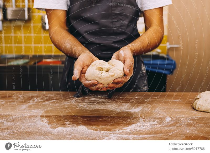 Männlicher Bäcker mit rohem Teig in einer Bäckerei kneten Teigwaren Mann Küche Inszenierung vorbereiten Küchenchef männlich Schürze Tisch Koch kulinarisch