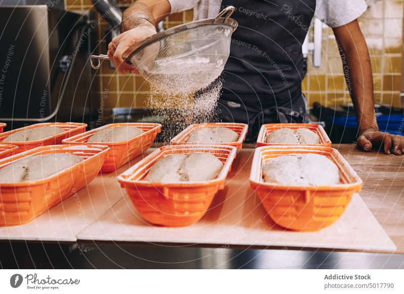 Männlicher Bäcker, der Mehl auf den Teig streut bestäuben Teigwaren Mann Koch Prozess Streuung Brot vorbereiten männlich Schürze roh Bäckerei Lebensmittel Küche