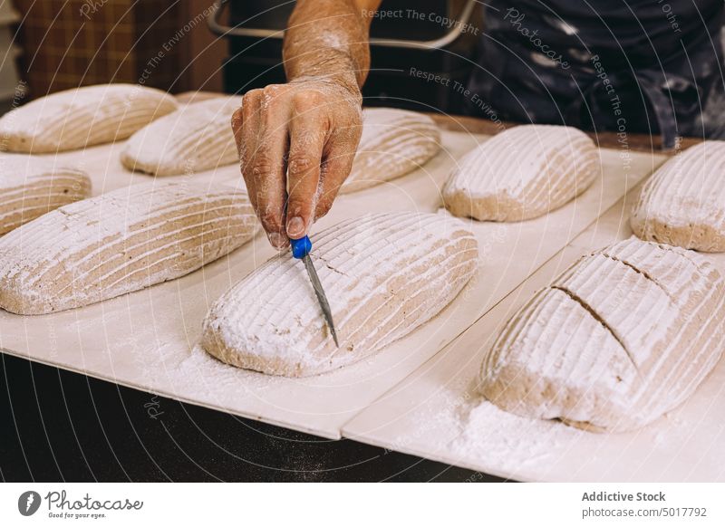 Männlicher Koch, der rohes Brot ritzt Bäcker Teigwaren Mann punkten Messer Prozess Brotlaib Bäckerei männlich vorbereiten Küche kulinarisch Lebensmittel frisch