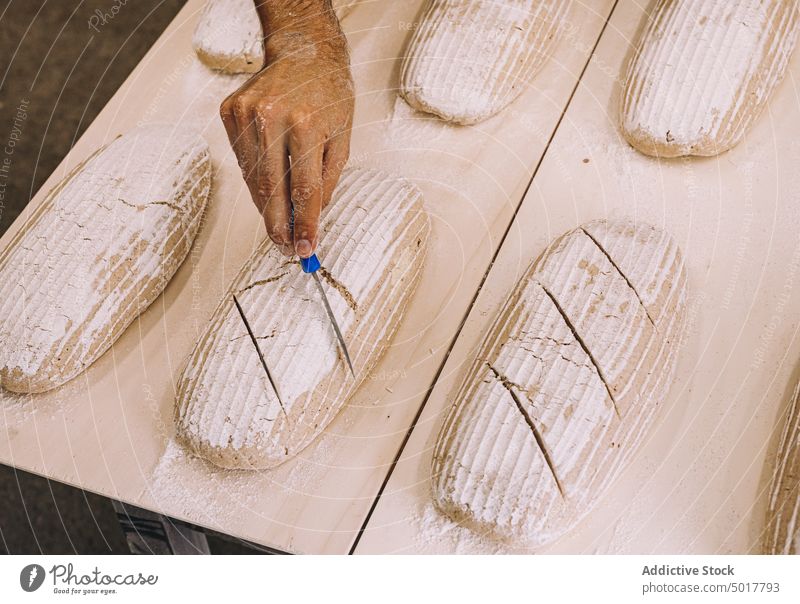 Männlicher Koch, der rohes Brot ritzt Bäcker Teigwaren Mann punkten Messer Prozess Brotlaib Bäckerei männlich vorbereiten Küche kulinarisch Lebensmittel frisch
