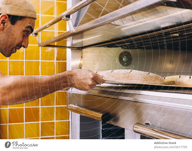 Mann beim Brotbacken im Backofen Bäckerei Ofen Koch Küche Teigwaren industriell männlich Tablett Schürze Gebäck vorbereiten Lebensmittel frisch kulinarisch