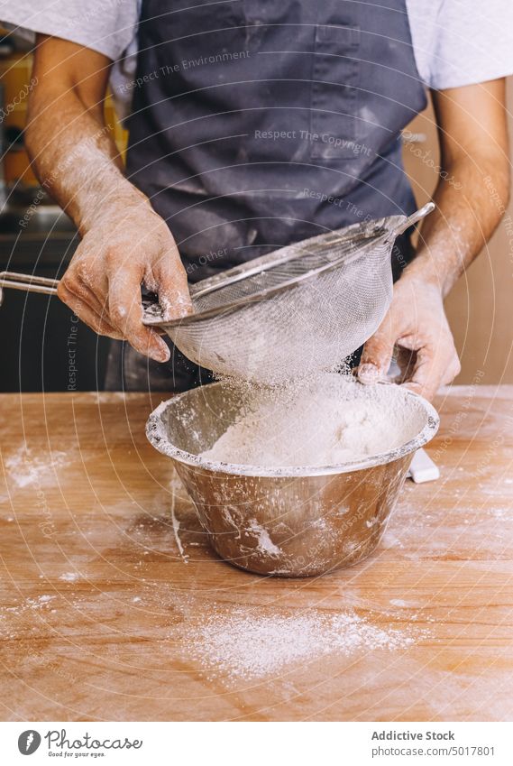 Kropf männlicher Koch siebt Mehl Sieb sieben Bäcker Mann Bäckerei Prozess Küche professionell Inszenierung vorbereiten Schürze hölzern Tisch Metall Küchenchef