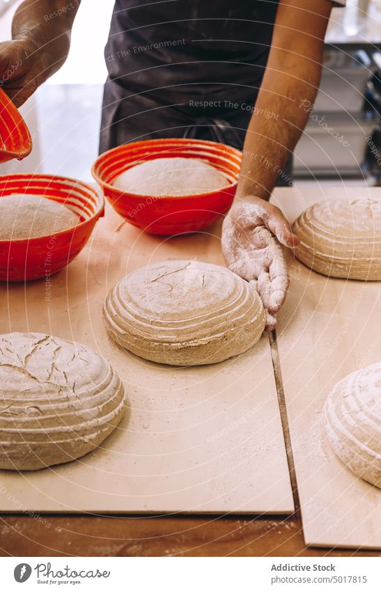 Männlicher Koch, der Teig mit einem Gärkorb formt Teigwaren vorbereiten Mann Bäcker Bäckerei roh Brot Form männlich Schürze hölzern Tisch Herstellung Prozess
