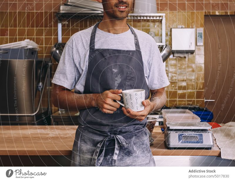 Männlicher Bäcker mit einer Tasse Kaffee Kaffeepause Mann Koch sich[Akk] entspannen genießen Erfrischung Schürze männlich hölzern Tisch dreckig fettarm Arbeit