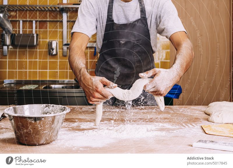 Anonymer Mann, der in einer Bäckerei Teig formt Teigwaren Koch Prozess Form vorbereiten Tisch Uniform männlich Küche Lebensmittel hölzern Gebäck frisch