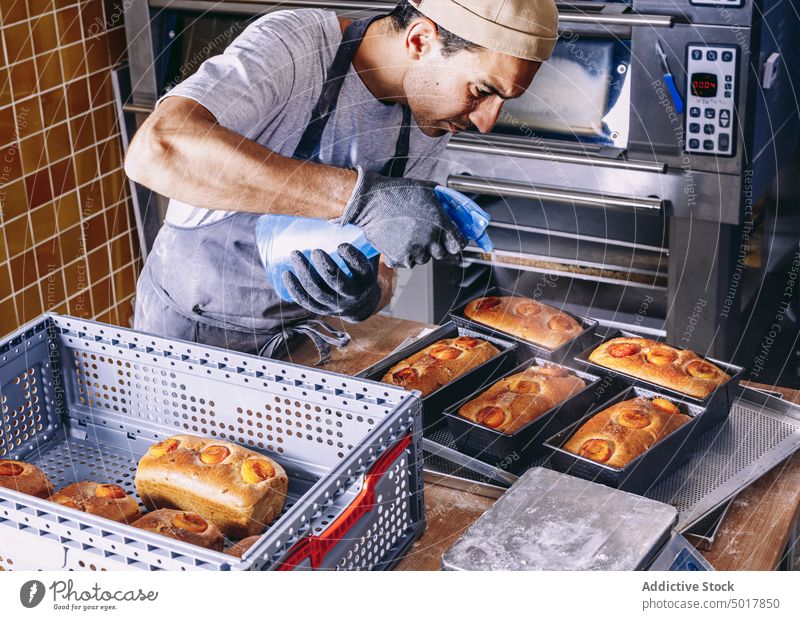 Männlicher Koch, der rohen Teig mit Wasser besprüht Bäcker Brot Prozess Mann Bäckerei Spray bestäuben Küche männlich Schürze vorbereiten Bestandteil kulinarisch